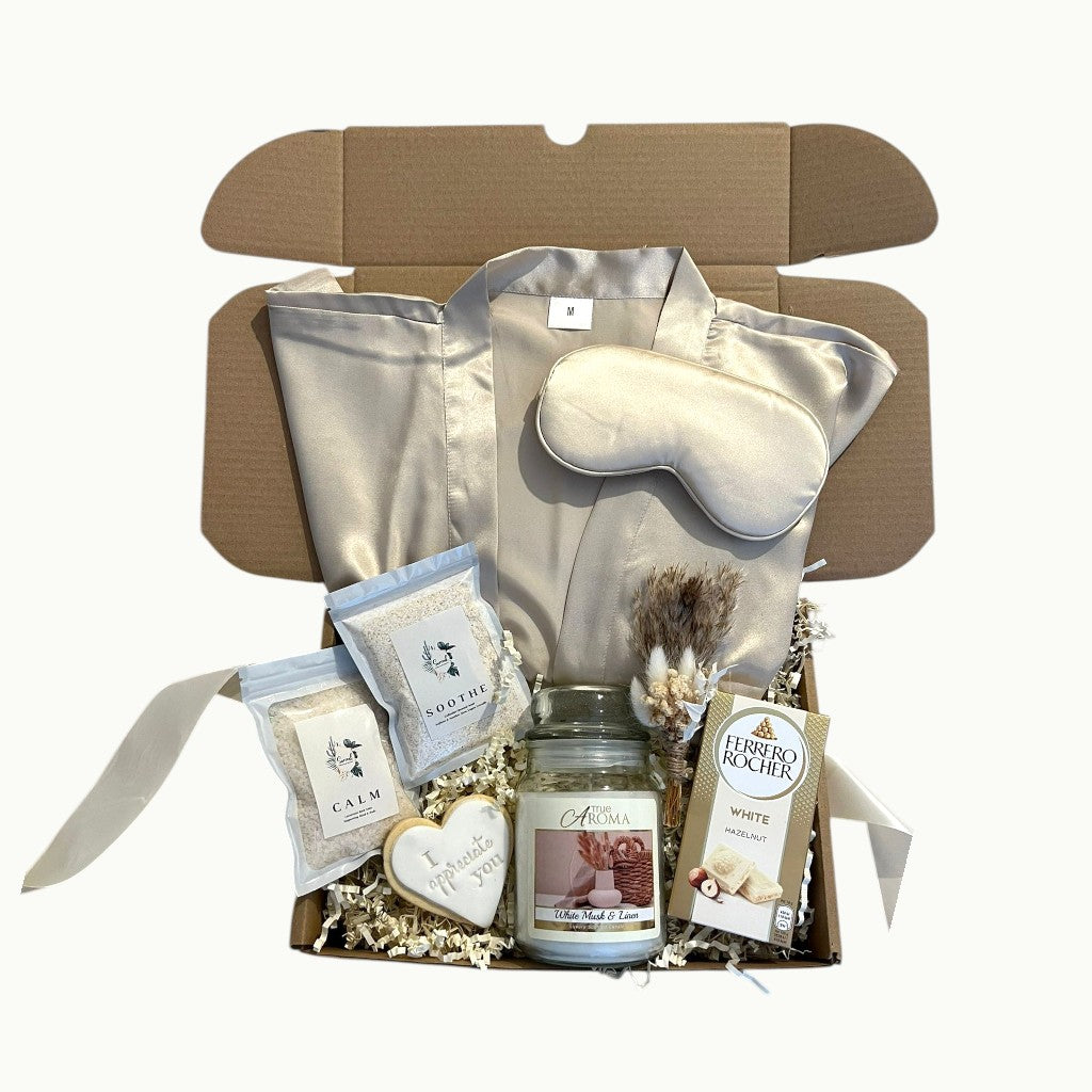 Luxury self care gift box with cream satin robe, silk sleep mask, bath salts, candle, hazelnut chocolate and personalised cookie, beautifully arranged in a pamper hamper