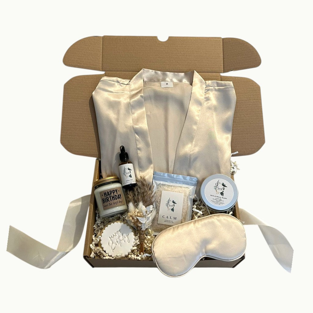 Luxury self care gift box with satin robe, silk eye mask, bath salts, candle, skincare and personalised cookie, arranged as a pamper hamper gift for her