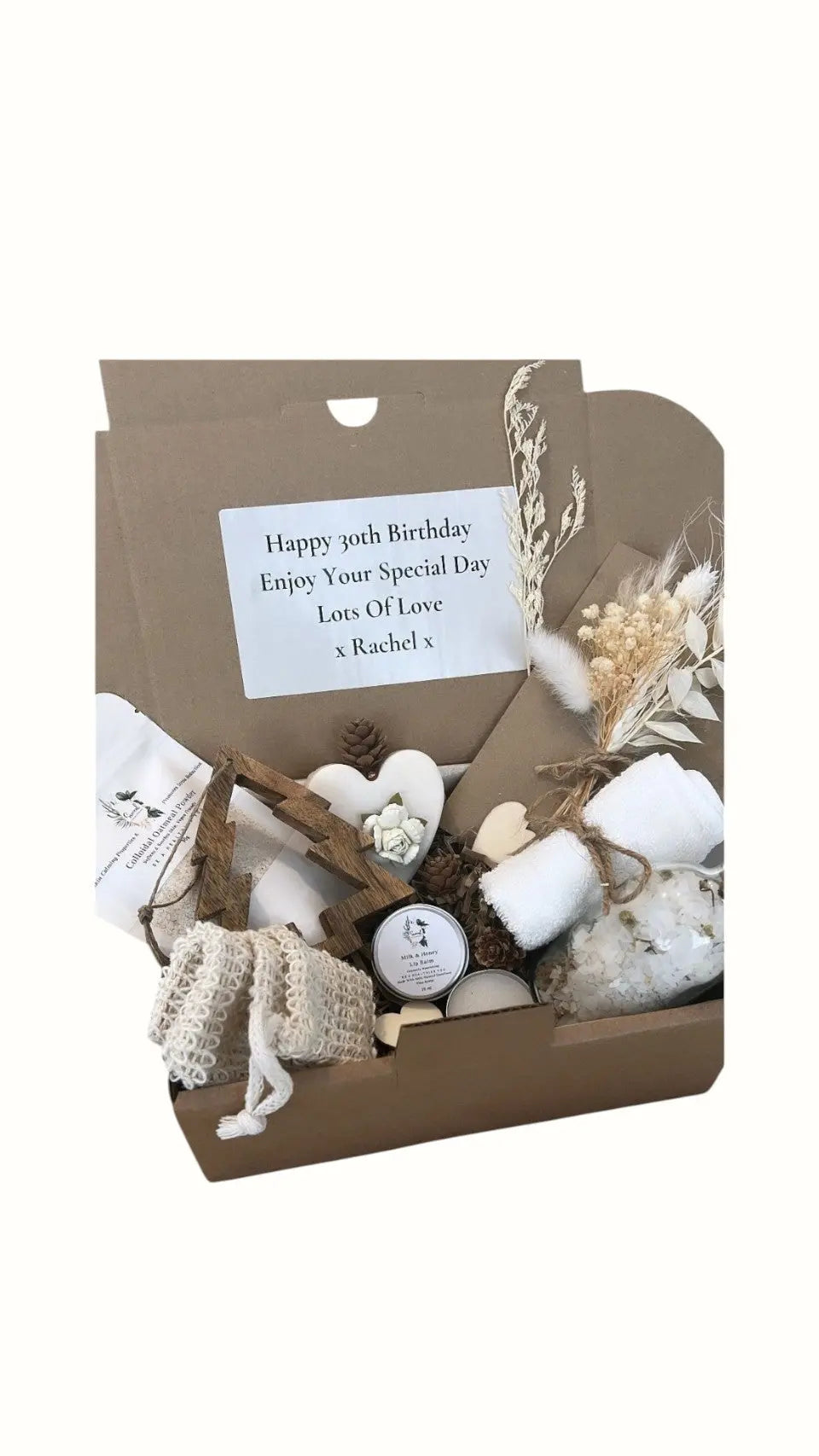 A gift box containing various skincare items including a soap bar, lip balm, clay mask, bath salts, and decorative elements with a personalized happy birthday message. Luxury Christmas Gift Box with Bath Salts and Candle