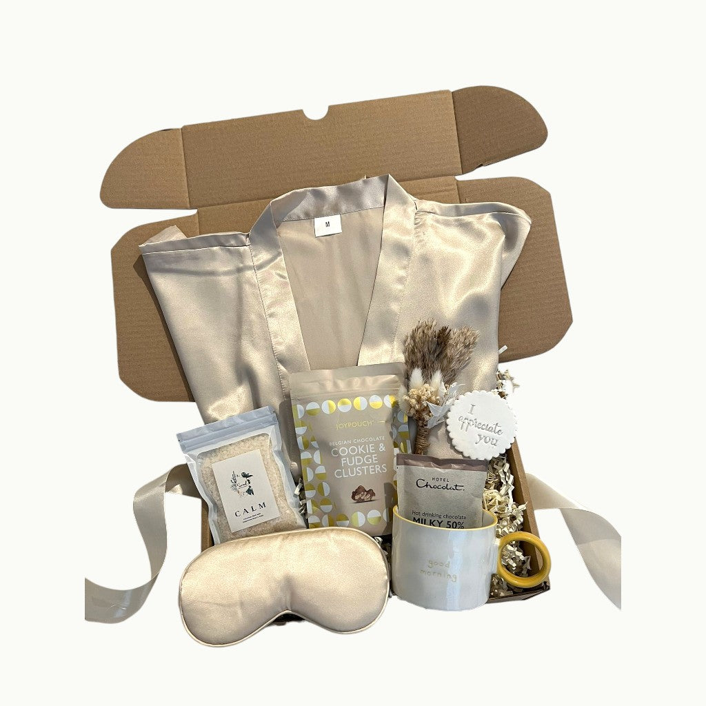 Gift box with a robe, sleep mask, mug, and other items on a white background