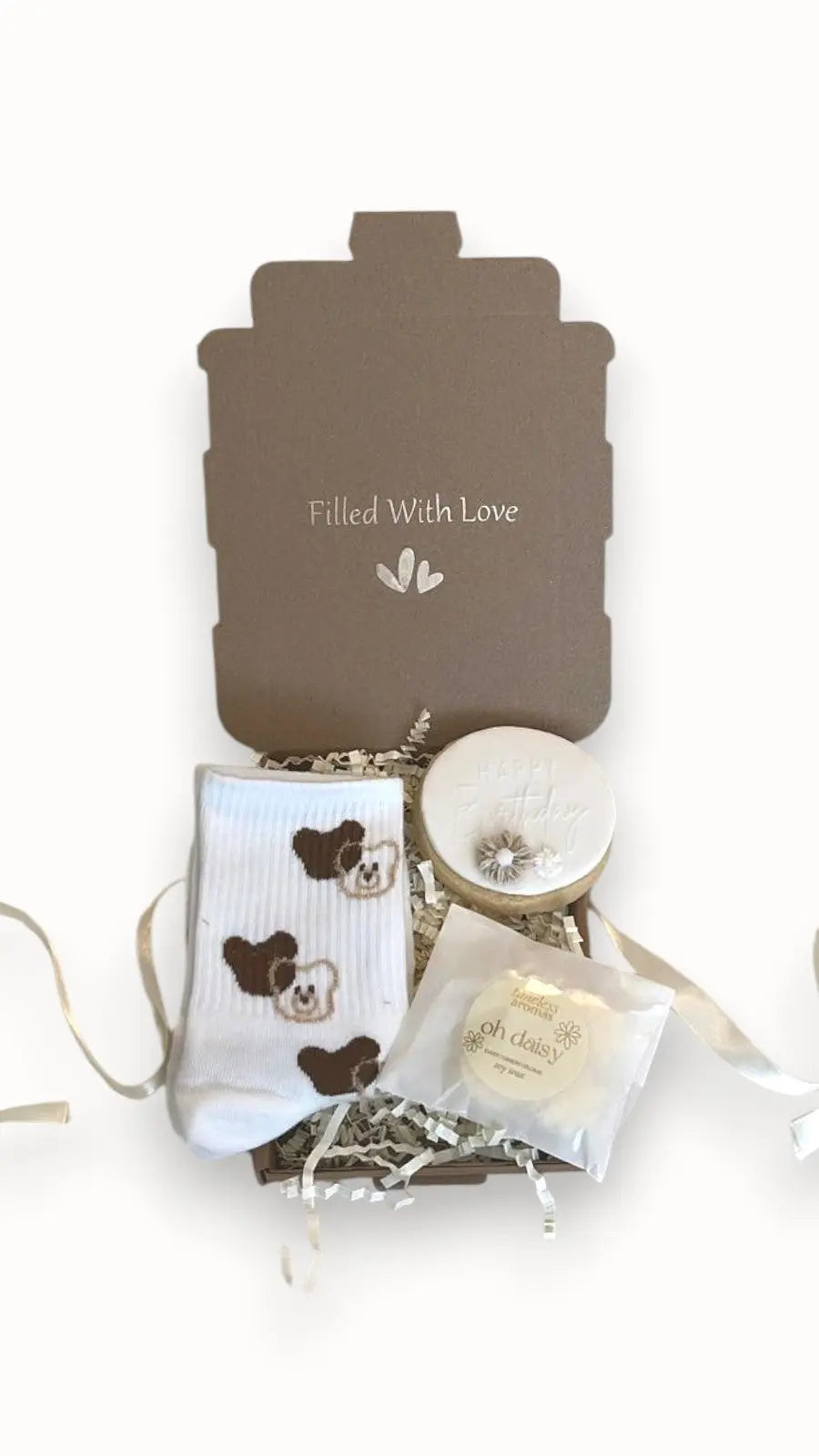 A gift set containing a pair of bear-themed socks, a happy birthday biscuit, and a heart-shaped necklace, all packaged in a box with a 'Filled With Love' card.
