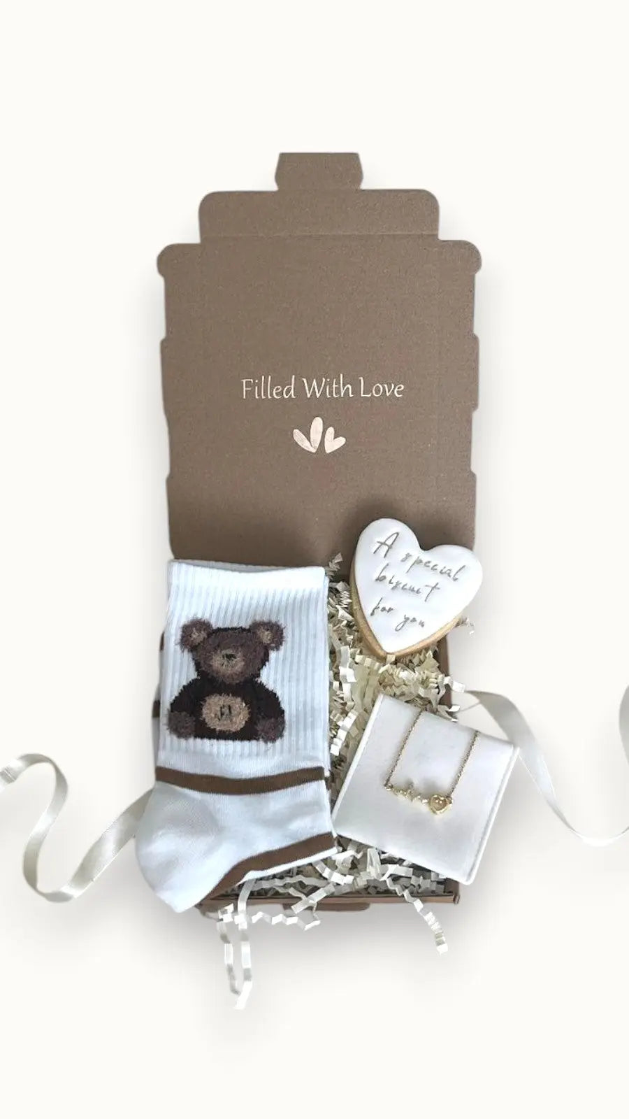 A gift box labeled 'Filled With Love' containing a pair of white bear socks, a special biscuit, and a love heart necklace.
Letter box gift