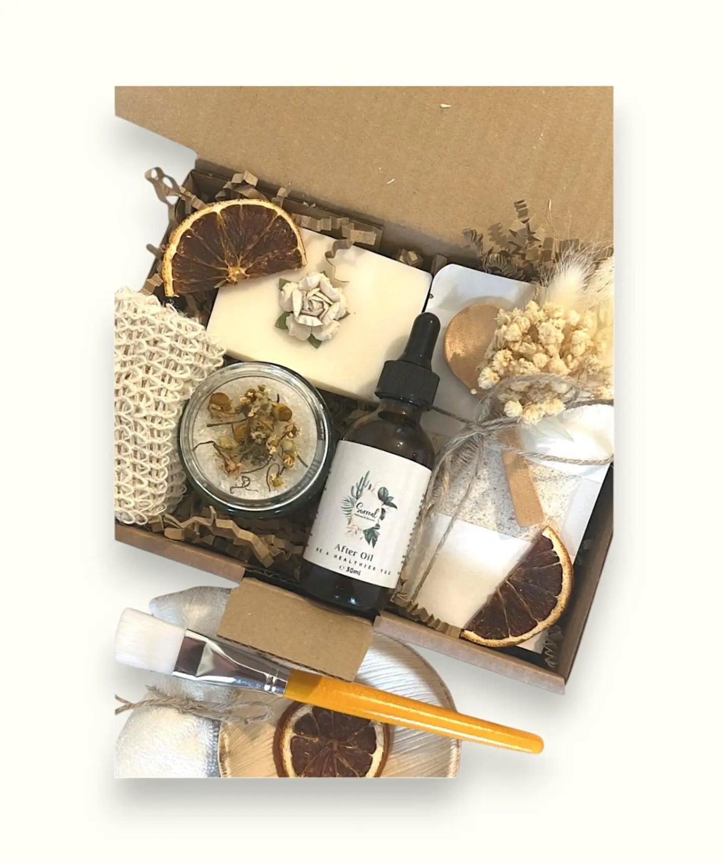 Vegan friendly hug in a box with natural skincare and sustainable pamper gifts including a candle, a soap bar, a bath soak, a bath salts, a towel, a dried flower, and a small bowl with a spoon.