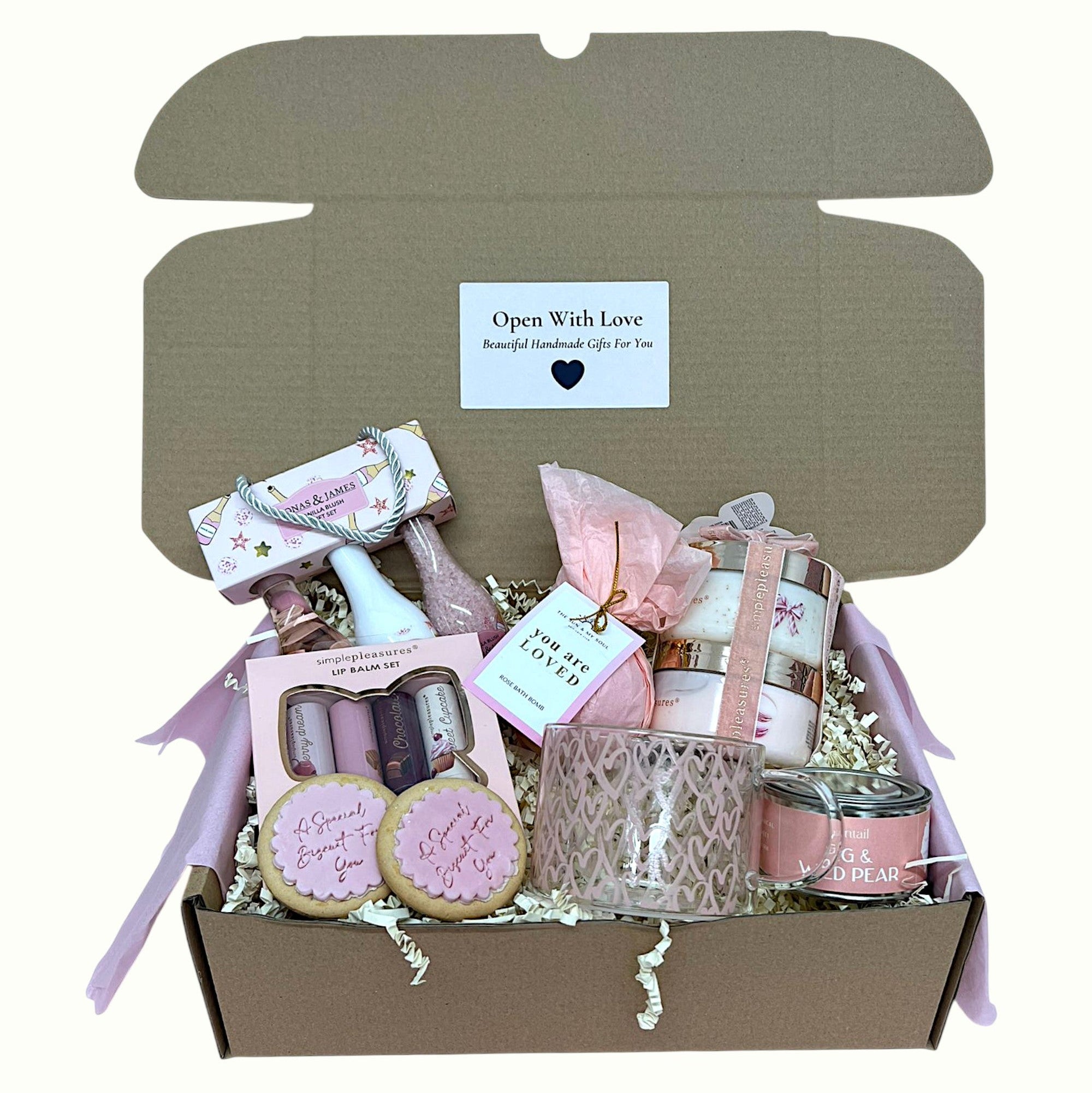 Gift box with pink and white items including cookies and a candle, on a white background.
