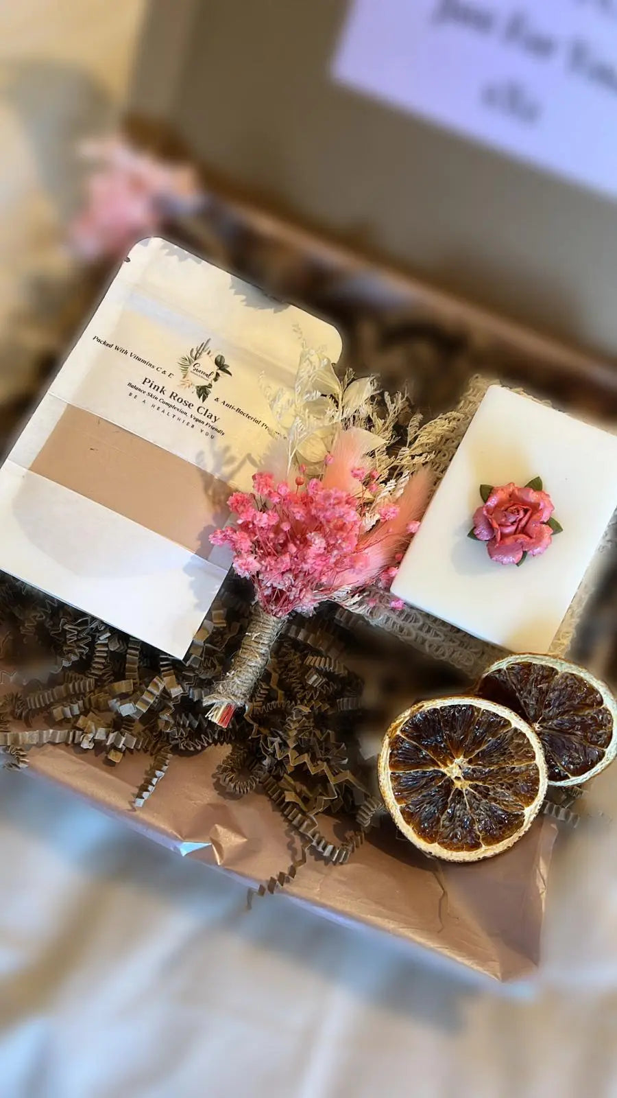 A gift box open to display a variety of skincare products including a soap bar, clay mask, exfoliation soap bag, and decorative dried flowers, all arranged on brown paper with a note that reads 'A Special Gift Just For You xx'. Thinking of you, hug for you, secret santa gifts for her