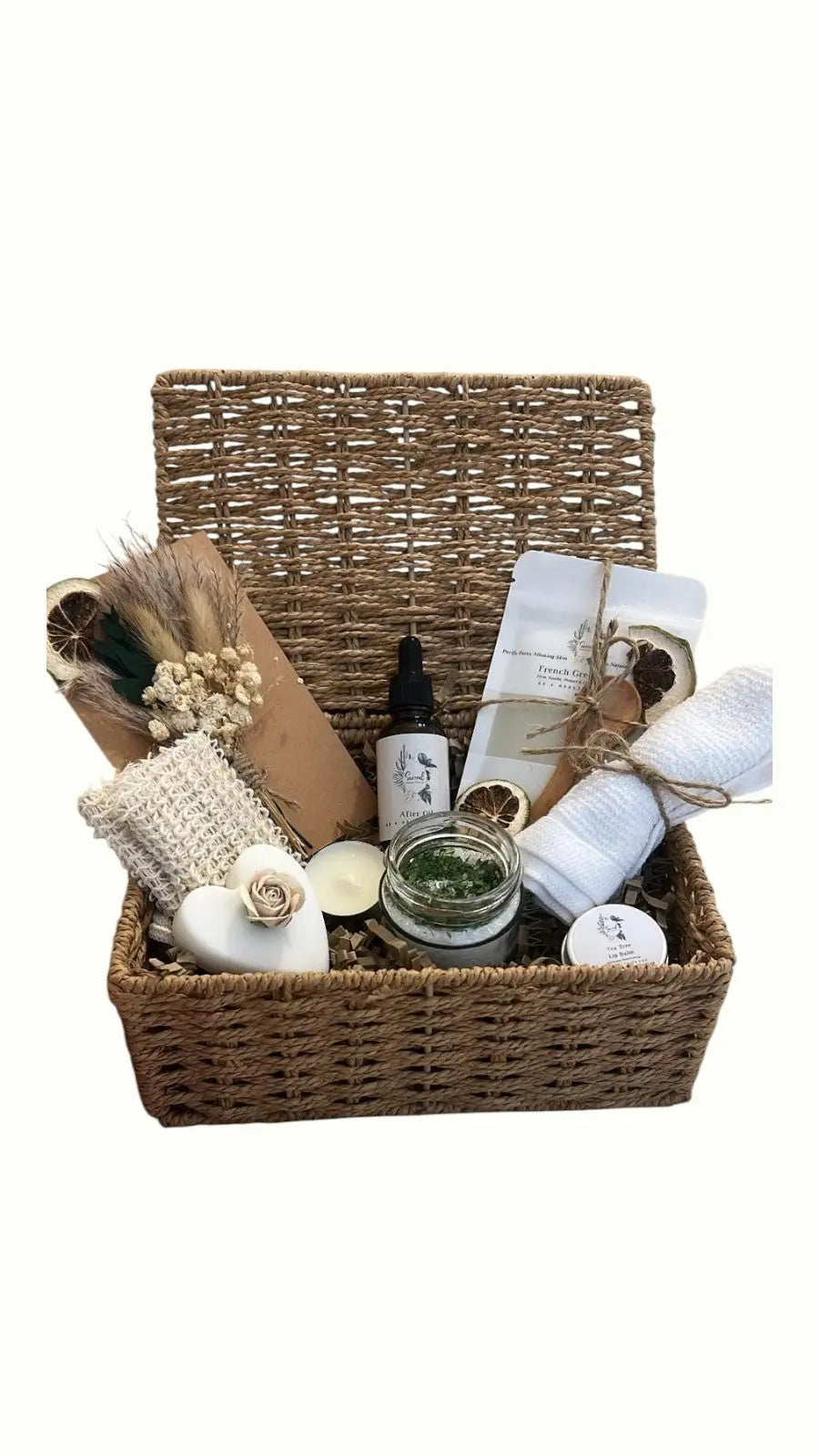 Wicker basket with various items including a After oil bottle, towel, and scrubber green clay mask. Wellness Hamper UK, Pamper Hamper UK, Curated gift boxes