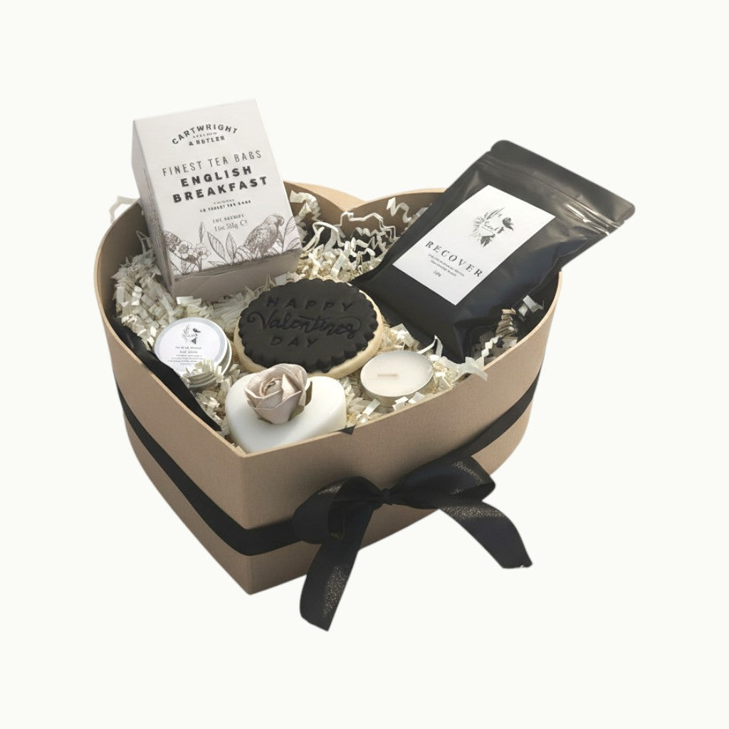 Heart-shaped gift basket with tea, cookies, and candles on a white background